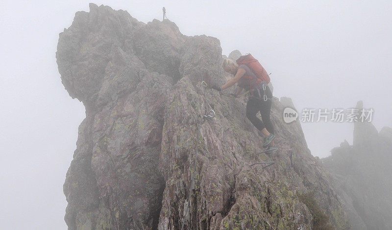 一个成熟的女人在雾中沿着岩石脊上的via ferrata移动